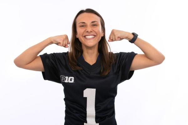 Young female posing in a football jersey flexing her arms with a smile on her face.