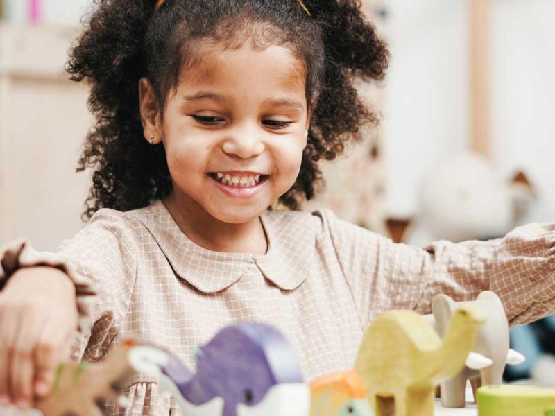 Selective Focus Photo of Smiling Young Girl Playing with Wooden Toys on White Table