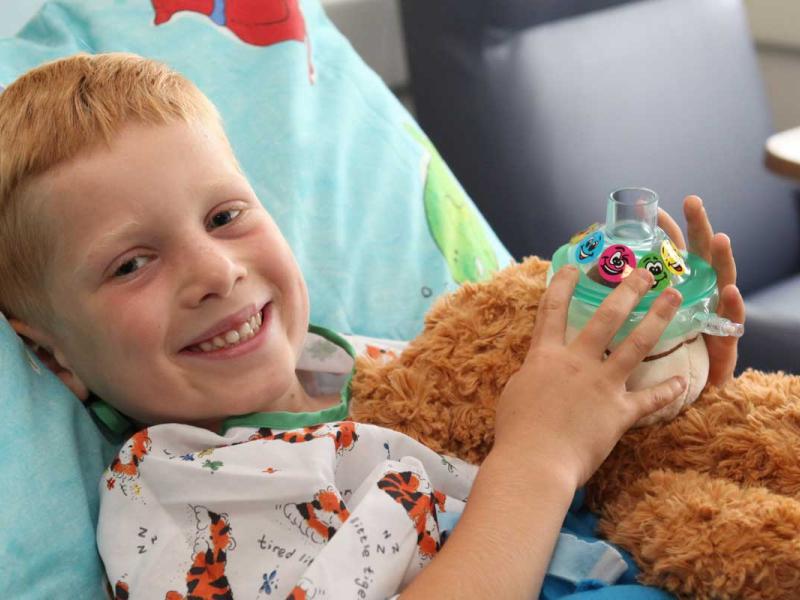 Young boy laying in a hospital bed holding a teddy bear.
