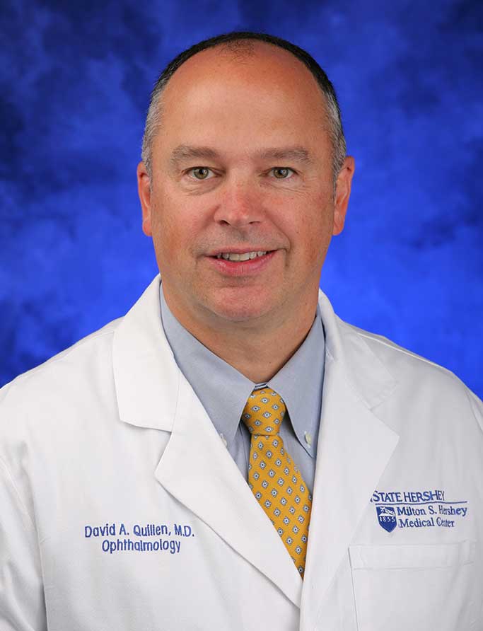 David Quillen, MD, is Chair of the Department of Ophthalmology at Penn State College of Medicine. He is pictured in a dress shirt, tie and medical coat against a blue background.