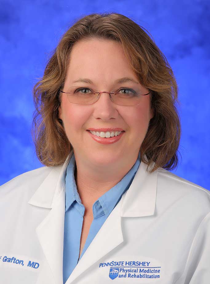 Lori Grafton, MD, is Interim Chair of the Department of Physical Medicine and Rehabilitation at Penn State College of Medicine. She is pictured in a blue dress shirt and white medical coat against a blue background.