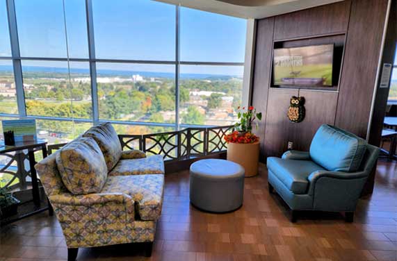 Ronald McDonald Family Room at Penn State Health Golisano Children’s Hospital with sofa, armchair, and large windows overlooking a scenic view.
