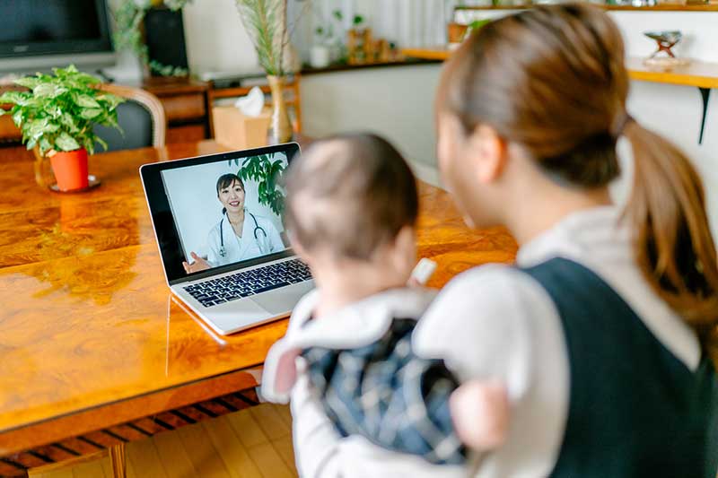 A mother with her baby is video calling a doctor on a laptop from home.