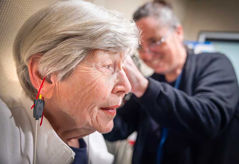 An audiologist fits a patient with hearing aids as she begins treatment for tinnitus.