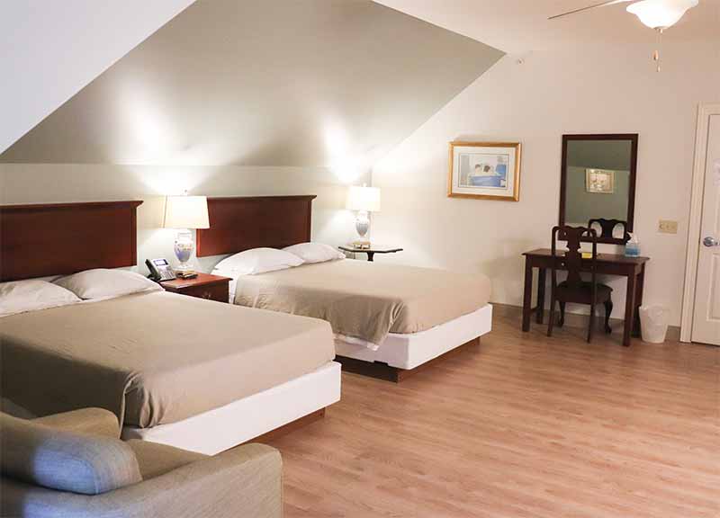Ronald McDonald House family guest room with two double beds, bedside lamps, a small desk with mirror and wood flooring.