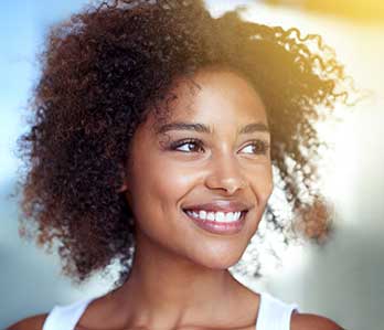 Close-up of woman with healthy, glowing skin smiling in the sunlight.