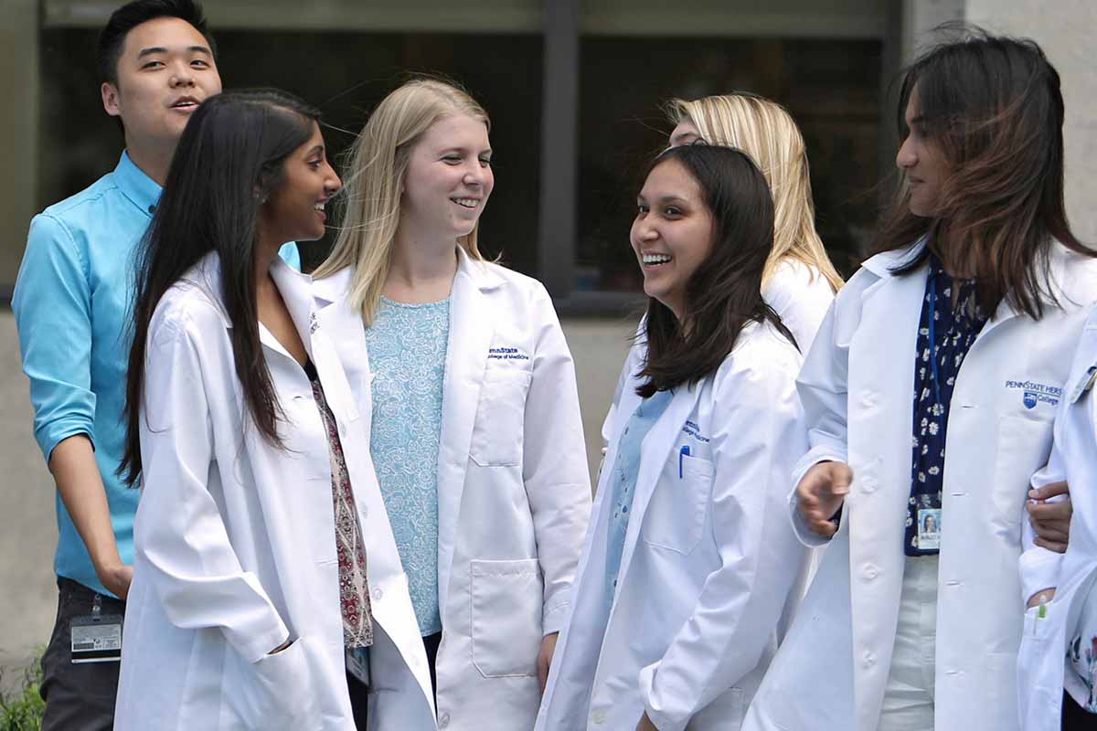 A diverse group of students in white coats gather outside of the College of Medicine. Photo taken in May 2018.