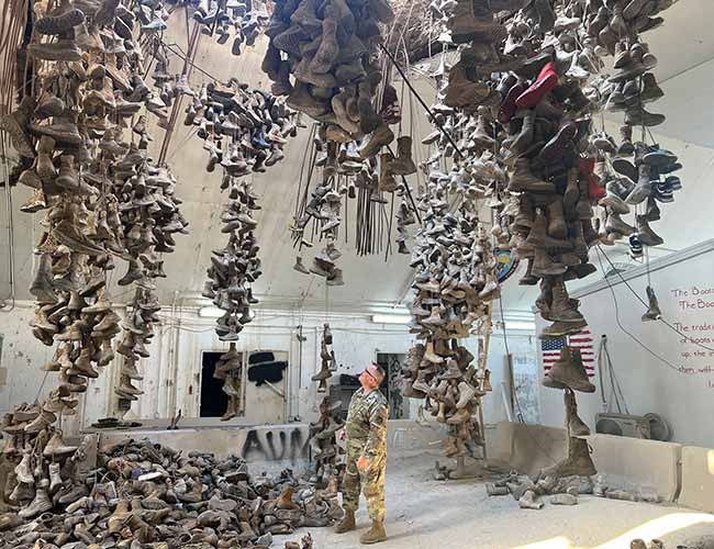 A U.S. soldier observes hundreds of worn boots hanging from the ceiling in the “Boots of Ali Al Salem” chandelier display