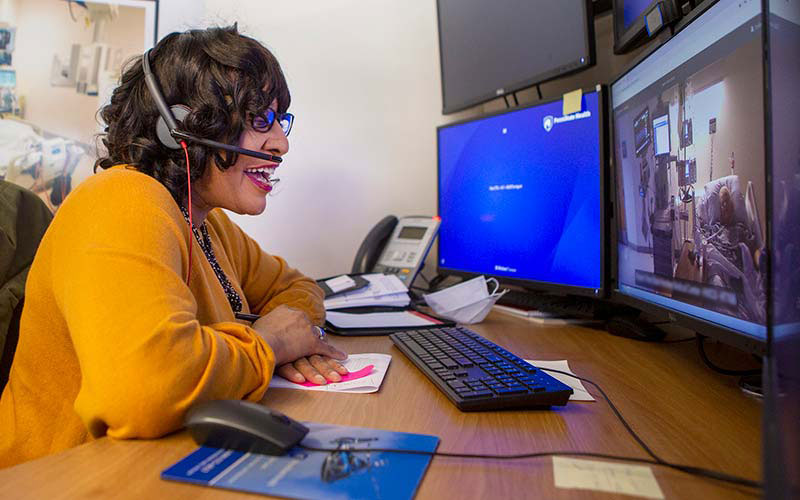Chaplain Darlene Miller Cooley with Penn State Health Milton S. Hershey Medical Center, communicates with a patient during a virtual visit on May 4, 2020. She is seated at a desk in front of four computer monitors. A patient is displayed on one of the monitors. 