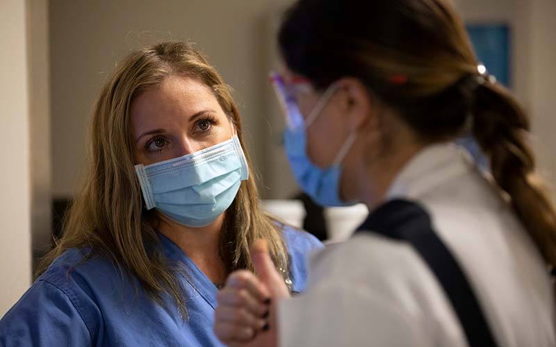 A registered nurse is pictured wearing a mask as she consults with a doctor in the Emergency Department. The doctor is also wearing a mask.