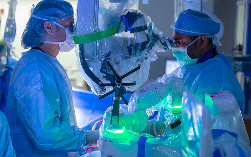 Two Penn State Health Milton S. Hershey Medical Center surgeons are pictured working with the Mazor X Stealth Edition Robotic Guidance Platform. Both surgeons are dressed in surgical gear.