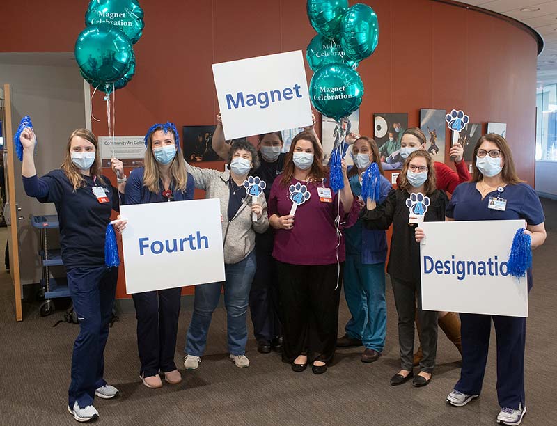 A group nurses posing with balloons and holding pompoms and signage stating fourth Magnet designation.