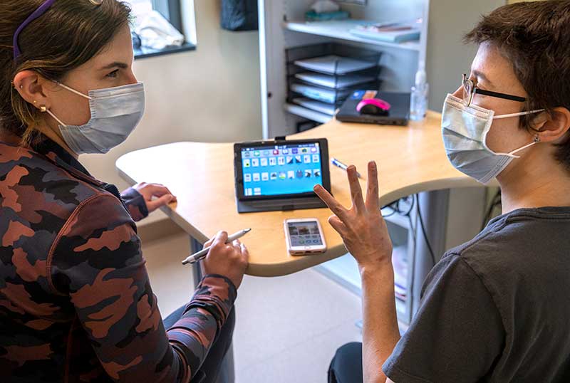 Speech-Language Pathologist assists adult patient in communicating with speech-generating device