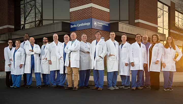 A group of cardiology care providers are standing outside in front of the Berks Cardiology building. They all are dressed in doctor coats.