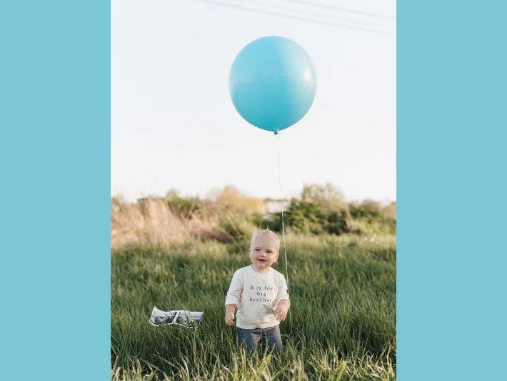 Toddler boy outside on a field, holding a large balloon floating above him.