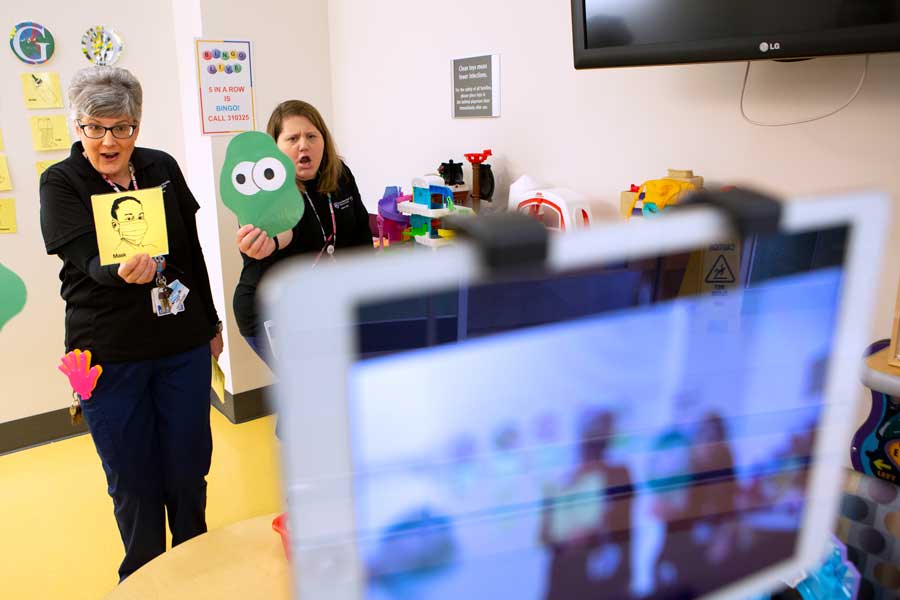 Two child life staff members playing virtual bingo with children online.