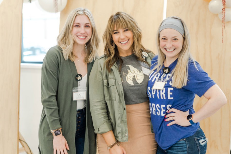 Courtney Kindrew, an RN with Penn State Health, wearing a light green jacket and a pink skirt, stands between two women during photo opp at a Rekindled Nurse workshop
