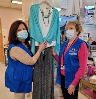 Two volunteers are standing with apparel hanging between them. Both volunteers are wearing medical face masks.