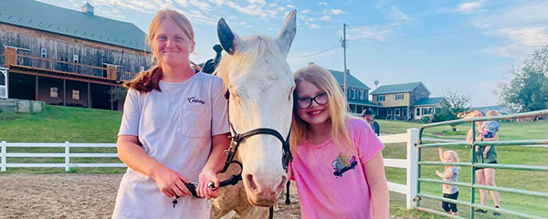 Two young girls holding a white horse in a riding arena.