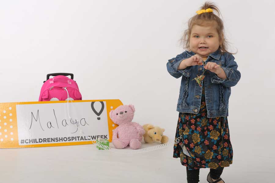 Young girl standing in front of children's hospital week sign smiling