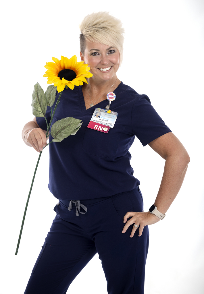 Photo of a woman holding a sunflower, wearing nursing scrubs.