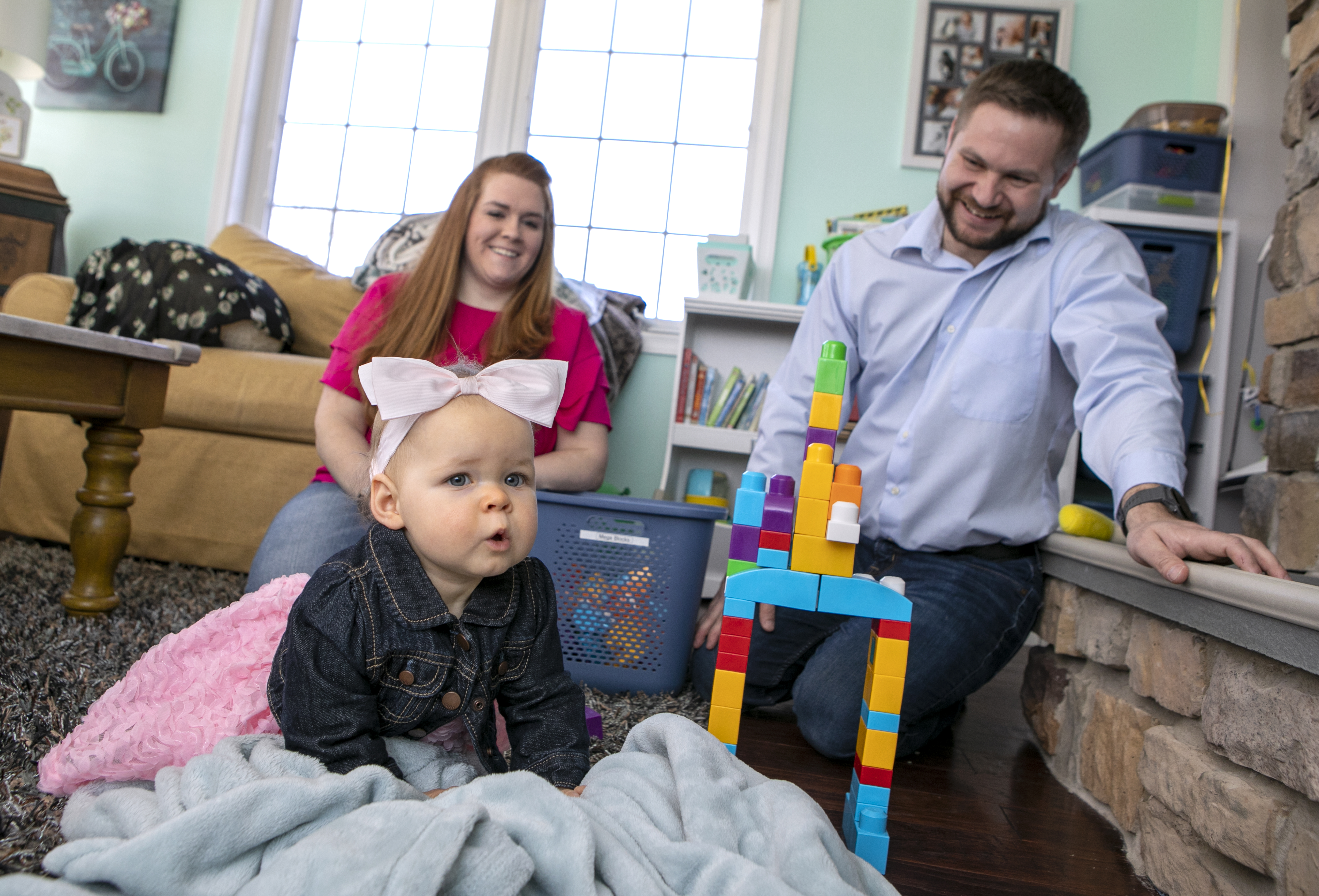 Penn State Health employees, Abbie and Peter Kostishak, sit on the floor smiling as they watch their infant daughter play.