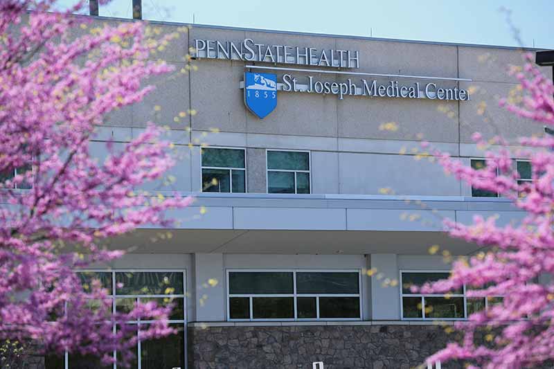The exterior of the Penn State Health St. Joseph Medical Center is framed by redbud trees in bloom in April 2017. A sign on the building includes the Nittany Lion shield with the year 1855 on it.