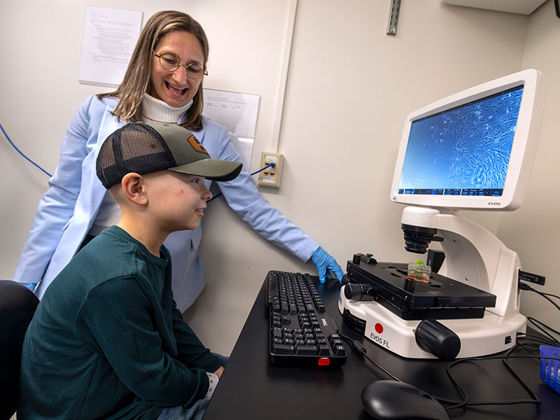 Young child sitting in front of a computer screen while a female is speaking to him about what's on the screen.