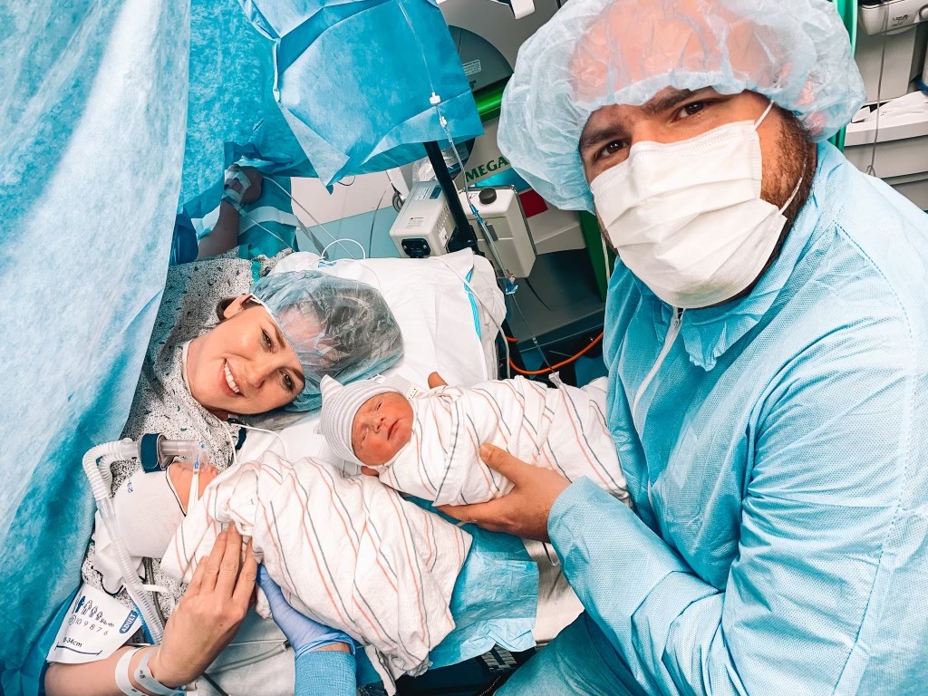 Young woman and man holding their newborn babies in an operating room setting.