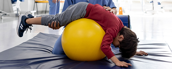 A boy has fun on an exercise ball during physical therapy.