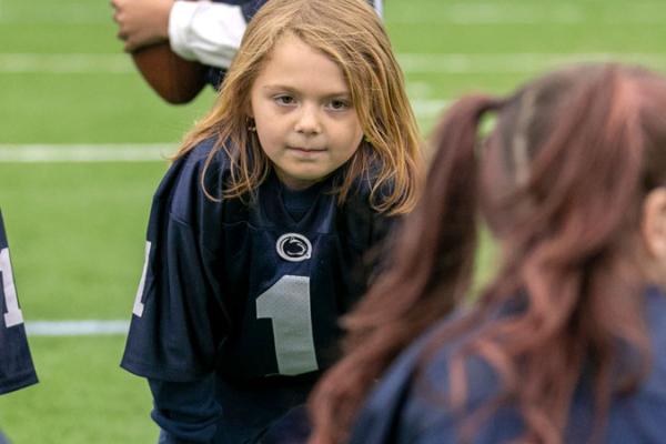 Young child on a football field and a dark blue jersey.