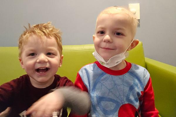 Two young male children are sitting on a green chair smiling and laughing together.