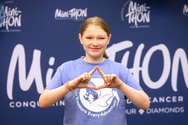 Image of a young girl standing in front of a mini THON banner.