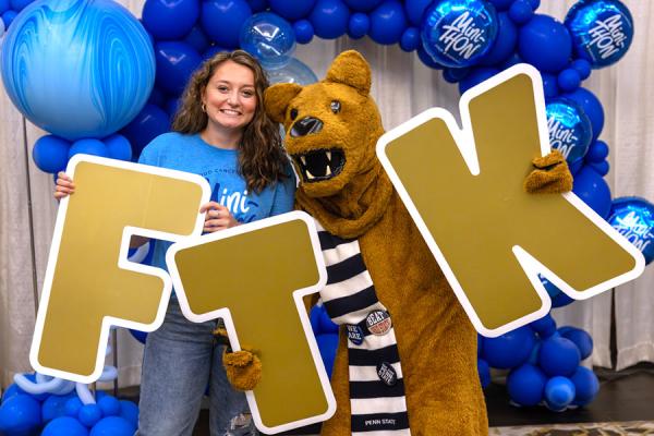 A young lady posing with Penn State Nittany Lion mascot holds the letters FTK which stands for For The Kids.