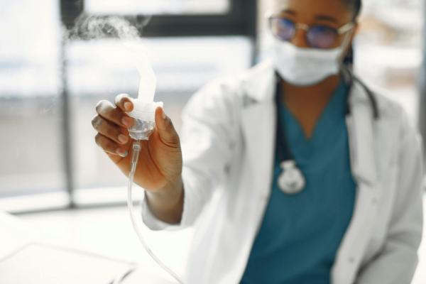 A female clinician is holding a medical device that has a white cloud of inhalant to treat a breathing problem. 
