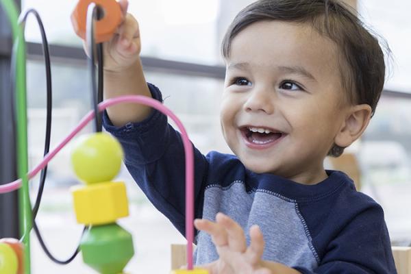 A toddler is playing with a toy that you can push shapes of plastic along metal tracks.