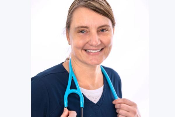 Young female posing in a dark scrub top with stethoscope around her neck smiling
