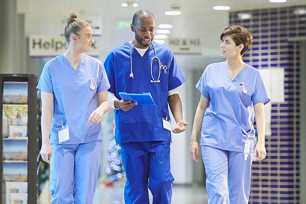 a medical consultant with two nurses walk along a hospital corridor