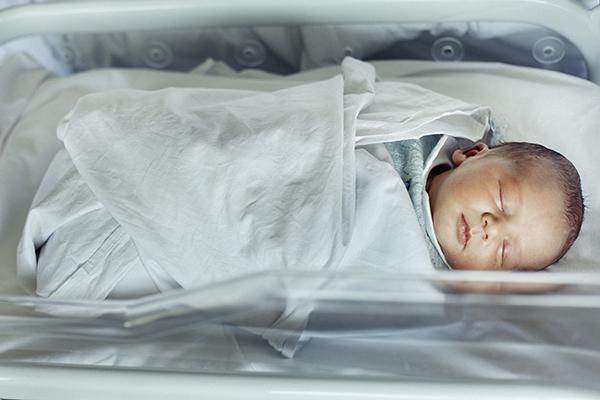 Newborn baby boy asleep in hospital bassinet.