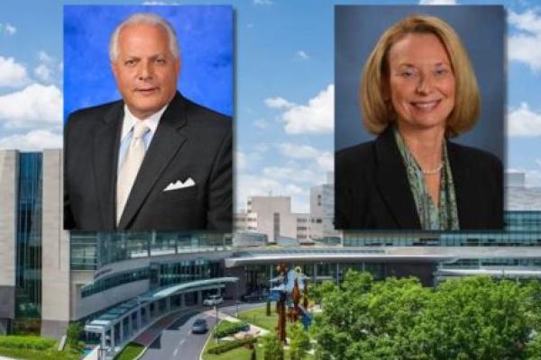 Composite image showing two professional headshots positioned above the entrance of a large modern hospital building. The headshot on the left features a man in a dark suit and light tie against a blue background. The headshot on the right features a woman in a dark blazer and patterned scarf against a gray-blue background. The hospital campus is visible below, with glass-fronted architecture, a circular drive, trees, and a partly cloudy sky.
