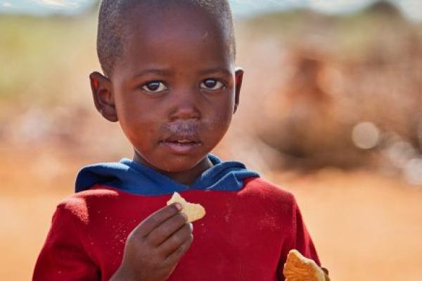A young boy in Africa eats a small piece of a biscuit.