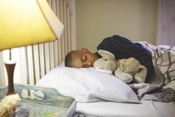 Boy holding a stuffed animal sleeping on a bed with a light on