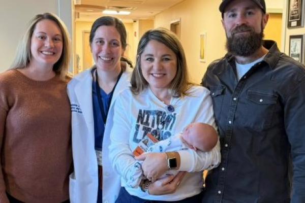 Three women and a man smile as they pose for a photo in the hallway of a doctor’s practice. From left, are Jamie Ober, registered nurse; Dr. Stephanie Estes, obstetrician-gynecologist; mother Jessica Hammaker holding a baby; and father, Justin Baer.