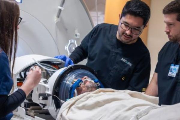 Medical team preparing a patient for a focused ultrasound procedure, with clinicians adjusting equipment around the patient’s head inside a specialized imaging device.