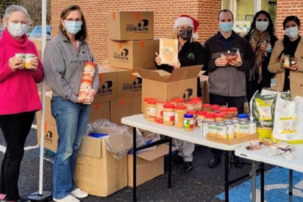 Six people hold food containers near a pile of boxes stationed in a parking space outside a brick building.
