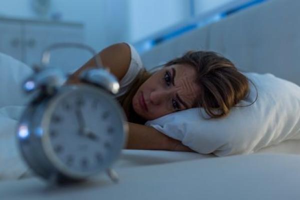 Woman with insomnia lying in bed looking at alarm clock.