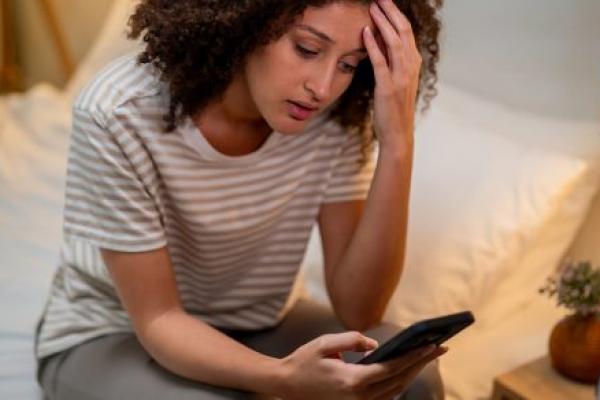 Stressed woman uses mobile phone as she sits on bed at night.