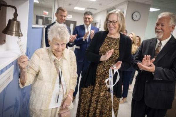 An older woman smiles as she rings a ceremonial bell mounted on the wall of the new Penn State Health Cancer Center at Hampden Medical Center.