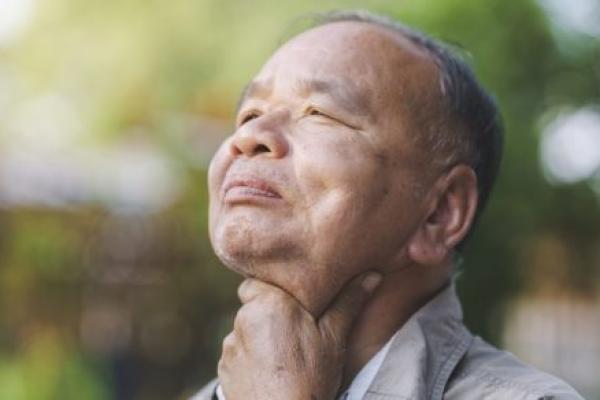 An elderly man holds his sore throat.