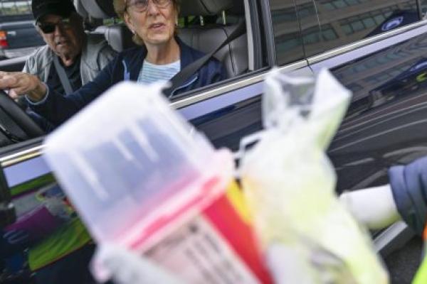 A man and woman sitting in a car talk to a person at Penn State Health’s Prescription Drug Take-Back Day. The person holds a sharps container and is wearing a safety jacket and coat.